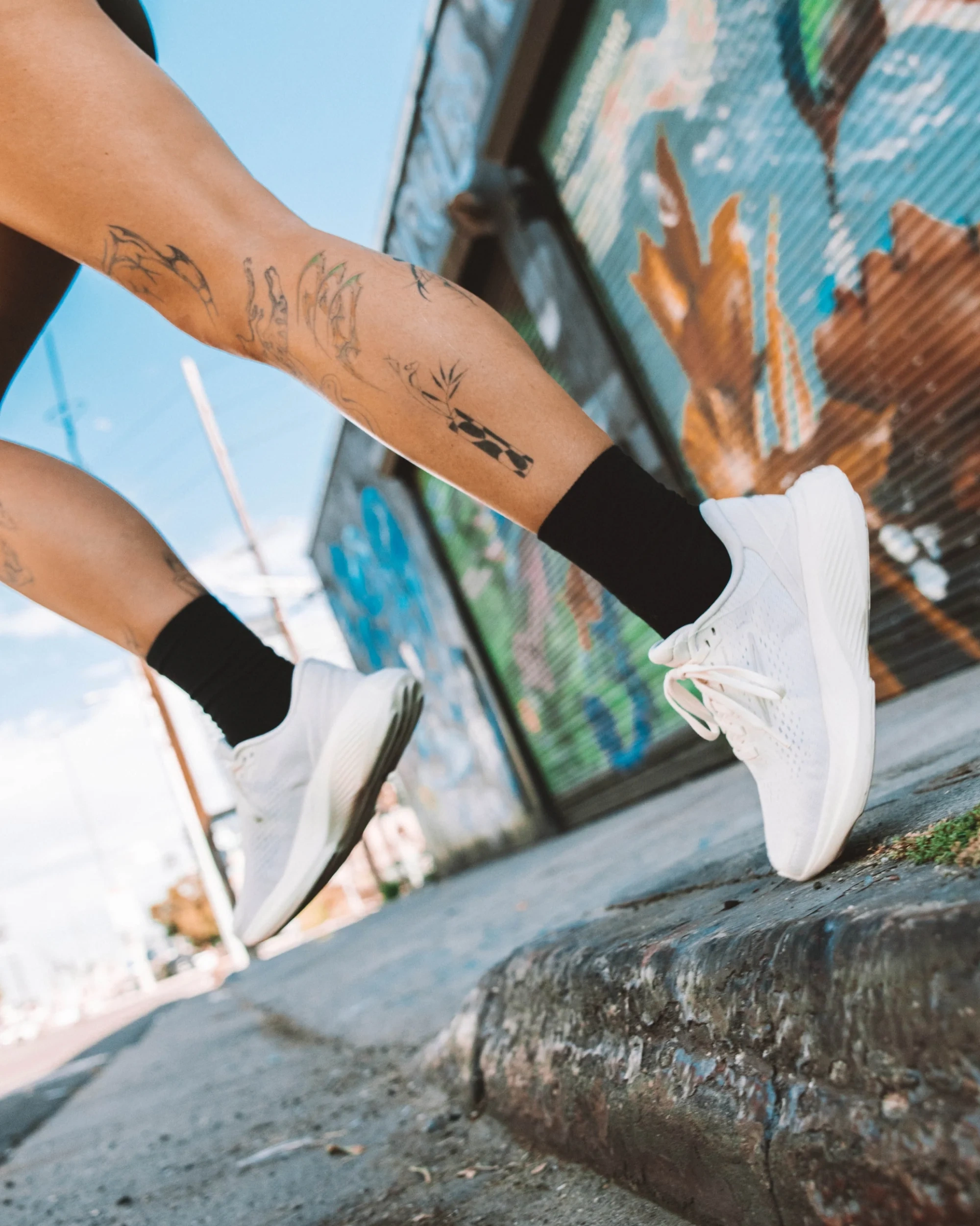 A runner in white hylo shoes steps off a kerb in front of a painted wall