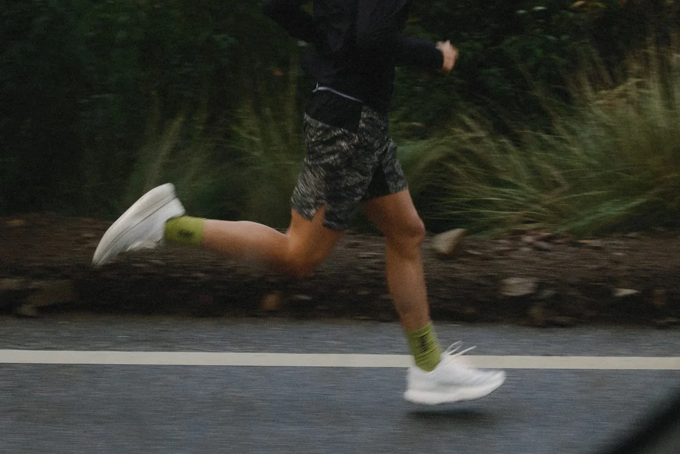 A runner in white hylo shoes passes a mossy wall at speed