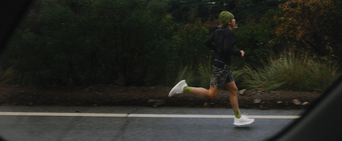 A runner at full stride on a dark roadside, seen from a passing car