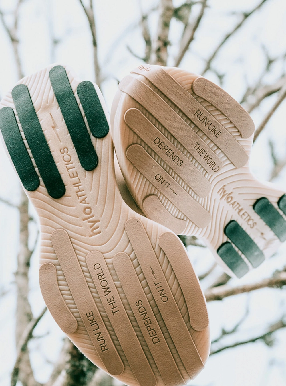 The sand-coloured outsoles of a pair of hylo shoes, with green rubber panels